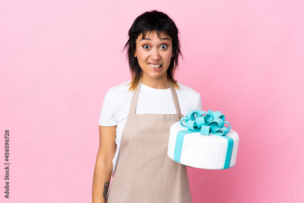 Uruguayan Pastry chef holding a big cake over isolated pink background having doubts and with confuse face expression Uruguayan Pastry chef holding a big cake over isolated pink background having doubts and with confuse face expression