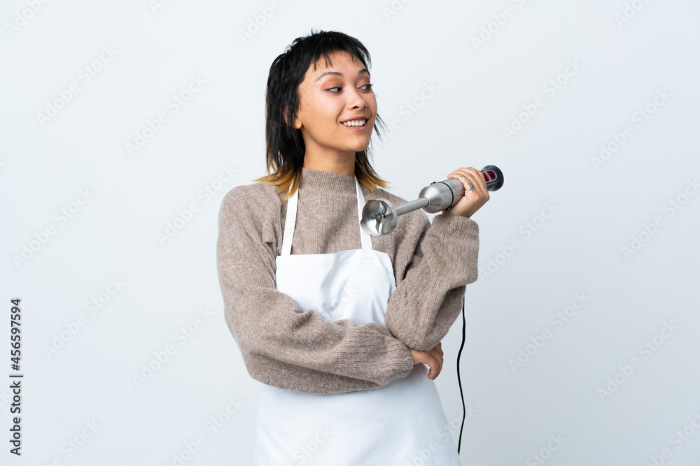 Chef Uruguayan girl using hand blender over isolated white background looking to the side Chef Uruguayan girl using hand blender over isolated white background looking to the side