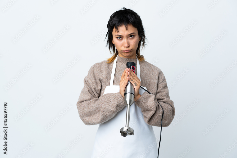Chef Uruguayan girl using hand blender over isolated white background pleading Chef Uruguayan girl using hand blender over isolated white background pleading