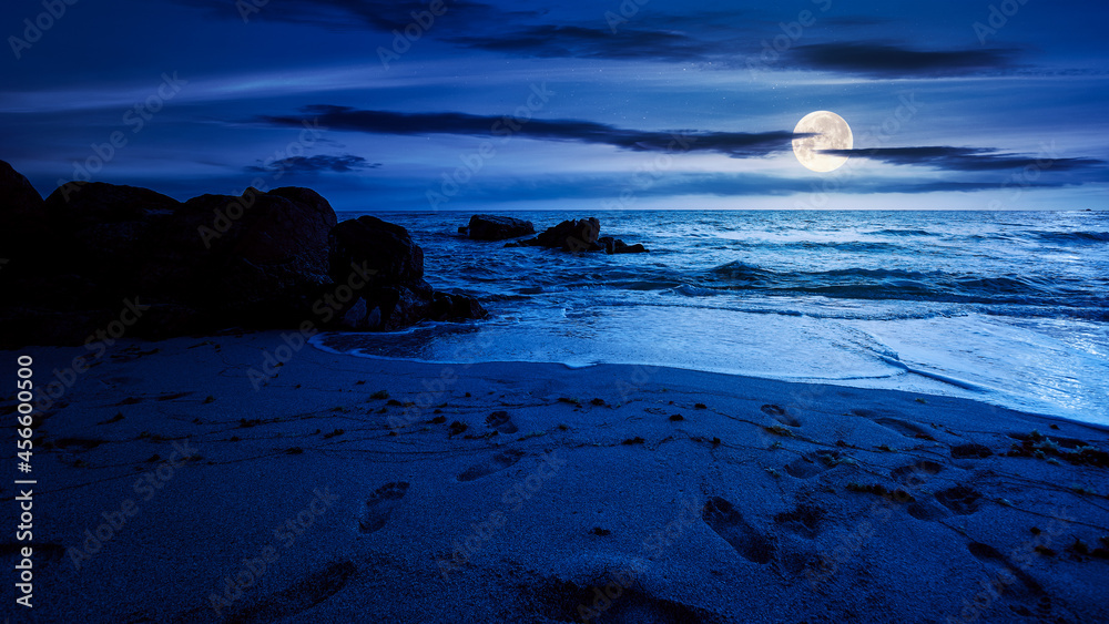 huge stones on the sandy beach at night. wonderful velvet season vacation on the black sea in full moon light. calm waves washing the shore. clouds on the dark blue sky above horizon