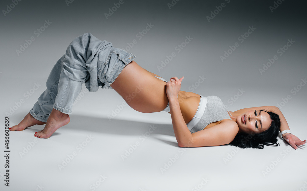 Young sexy brunette posing lying down in underwear and jeans on a gray background. The perfect athletic figure.