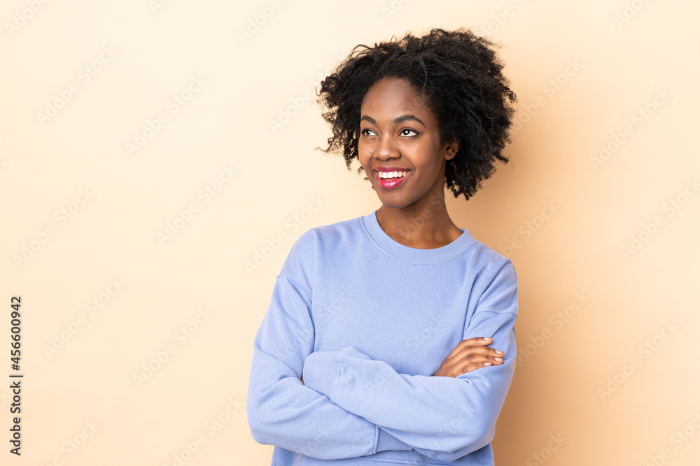 Young African American woman isolated on beige background looking up while smiling Young African American woman isolated on beige background looking up while smiling