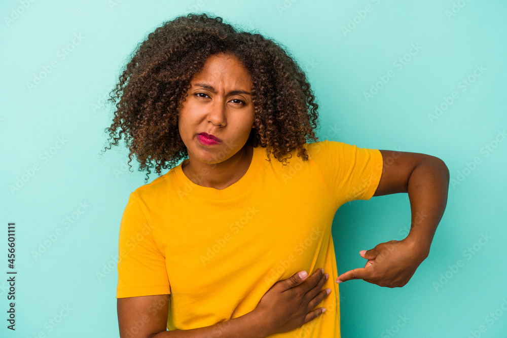 Young african american woman with curly hair isolated on blue background having a liver pain, stomach ache. Young african american woman with curly hair isolated on blue background having a liver pain, stomach ache.