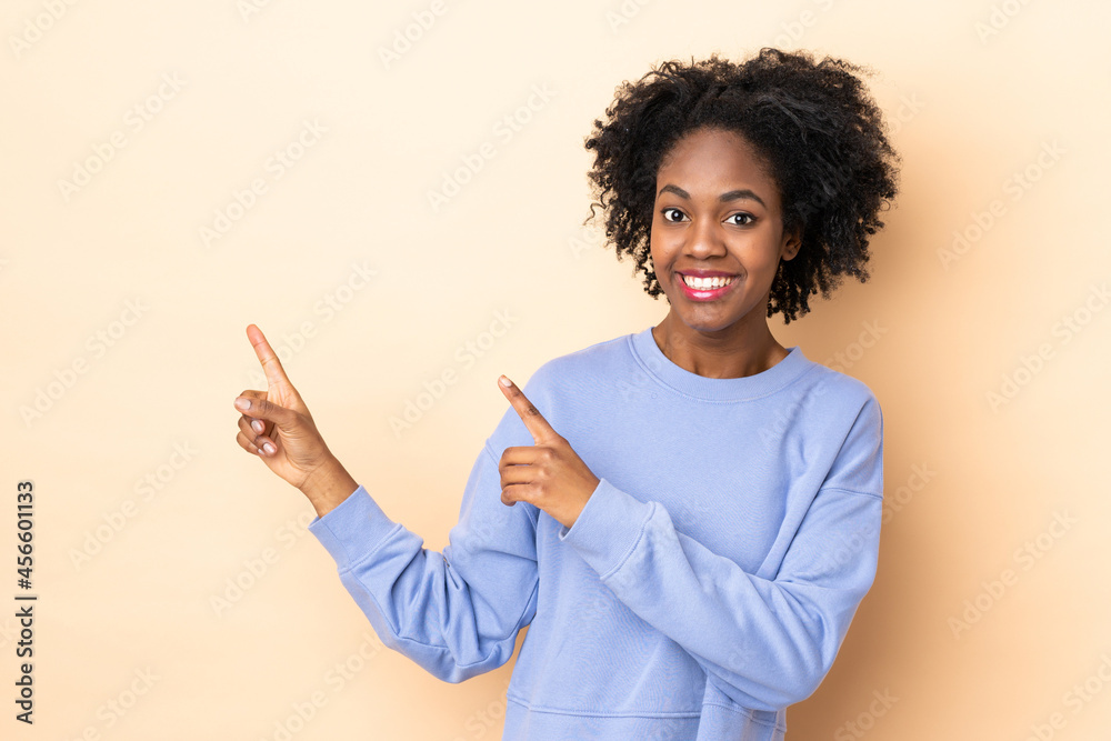 Young African American woman isolated on beige background frightened and pointing to the side Young African American woman isolated on beige background frightened and pointing to the side