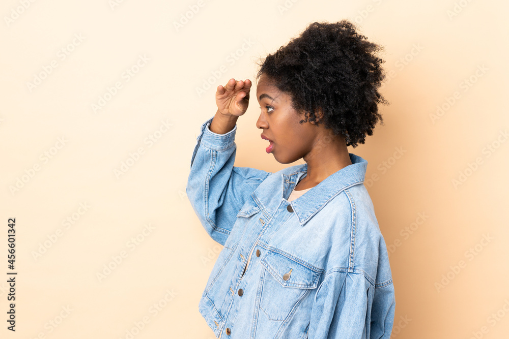 Young African American woman isolated on beige background with surprise expression while looking side Young African American woman isolated on beige background with surprise expression while looking side