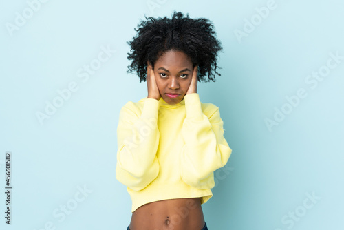 Young African American woman isolated on blue background frustrated and covering ears
