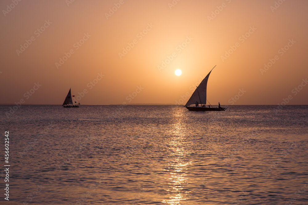 Two sailboats at sunset glide along the sparkling surface of the ocean in the rays of the setting sun