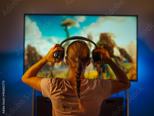 Girl with headphones watching TV. Close-up. Shooting from the back. Blue neon light. Rest, watching your favorite movies and TV shows, quarantine, relaxation, loneliness, insomnia. photo