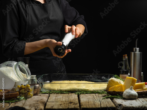 The chef sprinkles the dough with spices. He prepares traditional Italian bread focaccia. Ingredients. Wooden texture. Country style. Step by step recipe, culinary blog, recipe book.