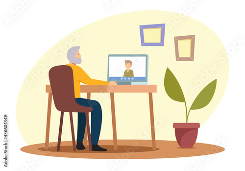Elderly People Hobby Concept. Senior Grey Haired Man Sitting at Desk with Laptop Chatting with Relatives via Internet