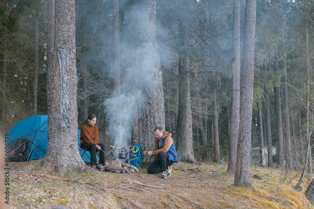 Fototapeta premium A married couple prepares food on a campfire on the shore of the lake with a tent.