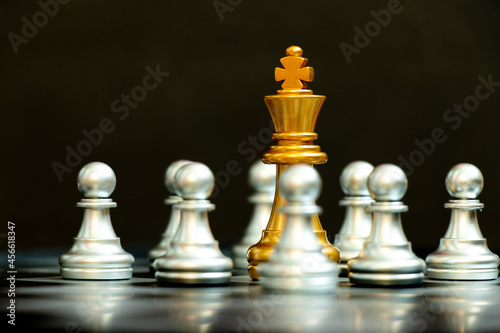 Gold king in chess game surrond with the another silver team on black background (Concept for company strategy, business crisis or decision)