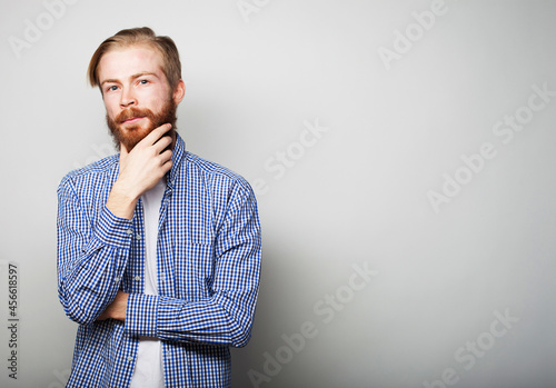 Handsome young bearded man in smart casual wear looking at camera, over grey background