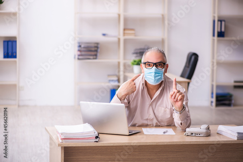 Old male employee working at workplace during pandemic