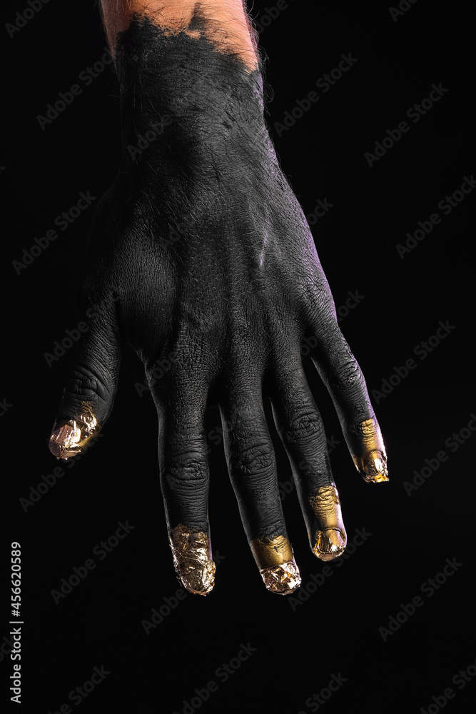 Fototapeta premium Male hand covered with black and golden paint on dark background