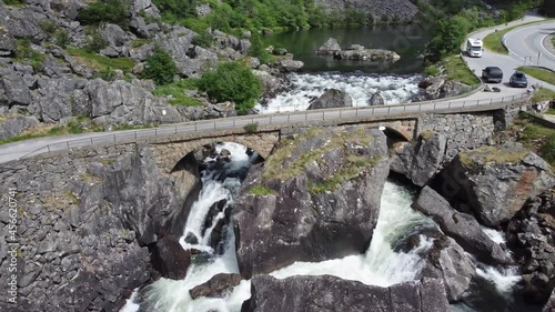 Road crossing old bridge built by rocks - River flowing from lake and below bridge - Mabodalen valley Norway aerial photo