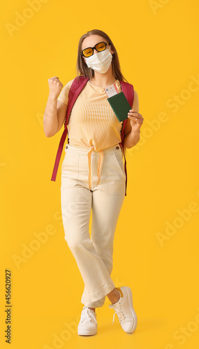 Happy female tourist in medical mask on color background