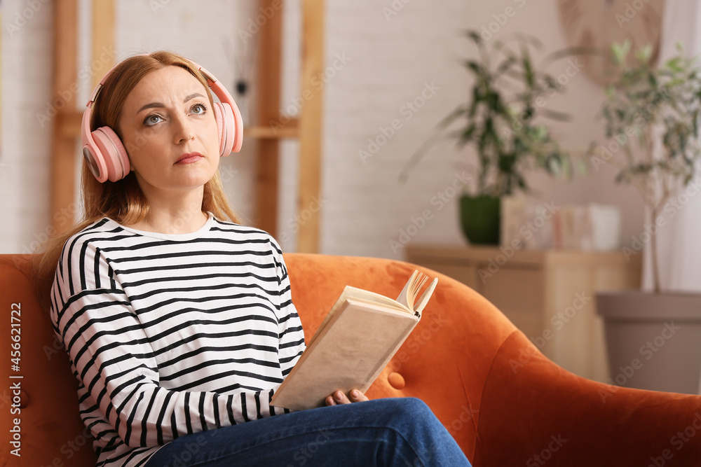 Mature woman with headphones reading book at home Mature woman with headphones reading book at home