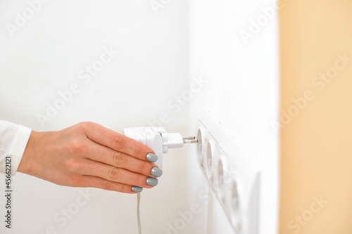 Woman putting plug into socket in room, closeup
