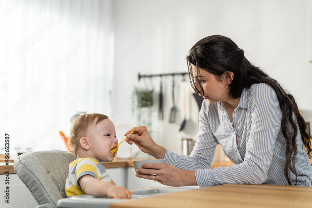 Caucasian beautiful mother take care of baby boy toddler in kitchen. Caucasian beautiful mother take care of baby boy toddler in kitchen.