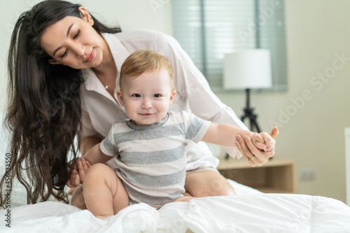 Caucasian loving mom play with cute baby boy child on bed in bedroom.