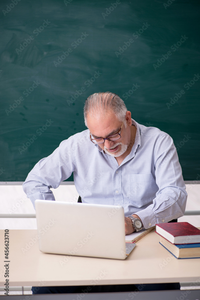 Old male teacher in front of green board Old male teacher in front of green board