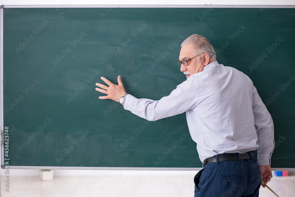Old male teacher in front of green board Old male teacher in front of green board