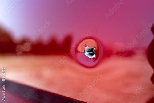 Close up shot of a bullet hole on within the passenger side door of a red car.