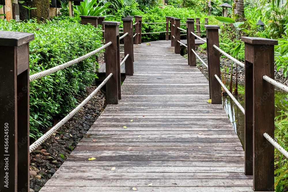 A dark wooden bridge crosses a pond in a tropical garden