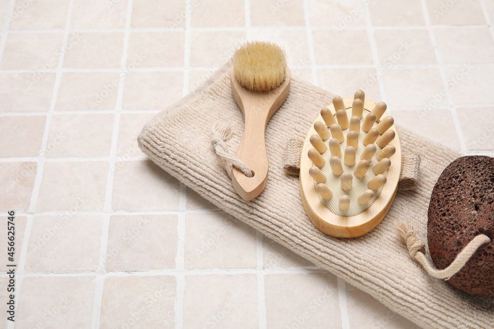 Different body brushes and towel on light tile background, closeup Different body brushes and towel on light tile background, closeup