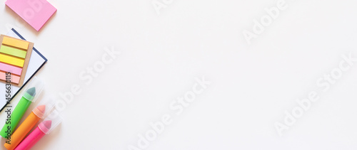 Banner with markers, stickers and notepad on a light white background. Colored office school supplies on the left side. Flatlay with copy space.