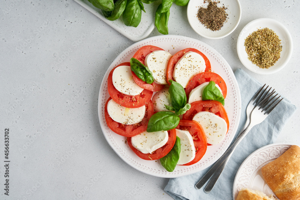 Horizontal flat lay of classic talian caprese salad with sliced tomatoes, mozzarella, basil, olive oil, pepper, salt and toast. Rustic mediterranean meal on light background. Copy space Horizontal flat lay of classic talian caprese salad with sliced tomatoes, mozzarella, basil, olive oil, pepper, salt and toast. Rustic mediterranean meal on light background. Copy space