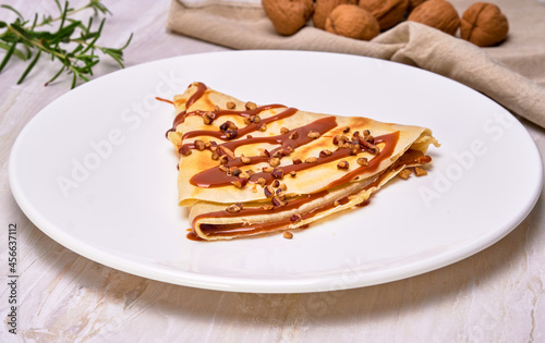 french crepes of cajeta (Dulce de leche) with walnuts on a white plate accompanied by walnuts on a brown cloth napkin. elegant concept. copy space for advertising.