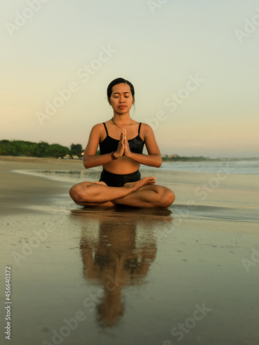 Yoga practice on the beach. Lotus pose. Padmasana. Hands in namaste mudra. Closed eyes. Meditation and concentration. Relaxation of body and mind. Yoga retreat. Sunset time. Seminyak, Bali © Olga