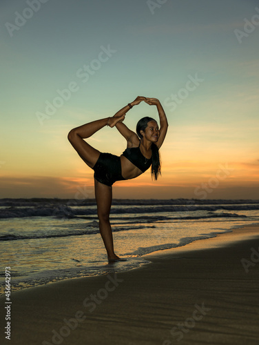 Sunset beach yoga. Slim woman practicing yoga, standing in Natarajasana, Lord of the Dance Pose. Balancing, back bending asana. Exercise on the beach. Seminyak beach, Bali