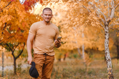 man in brown clothes with a smartphone stands in the autumn in the park