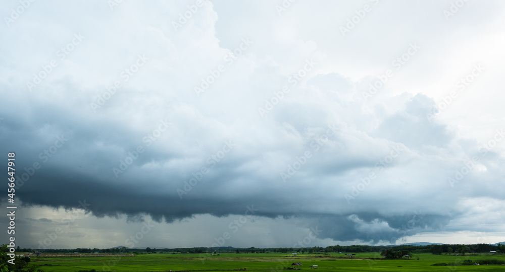 View of thunderstorm clouds above the rice field. Pouring rain and dark clouds over the pasture in countryside.