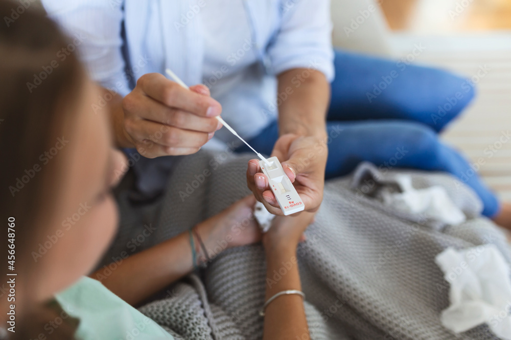 Obraz premium Mother is taking rapid covid-19 test at home to her sick daughter at home. Mother performing nasal swab on her child taking example to analyze if patient is positive for the infectious diseas