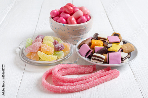 Chewy gummies, liquorice candies, fruit gum in bowls on a white wooden background. Holiday concept, baby treats. Unhealthy food.