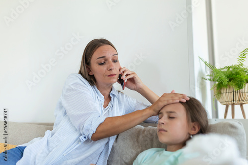 Mother measuring temperature of her ill kid. Sick child with high fever laying in bed and mother holding thermometer. Mother with cell phone calling to doctor