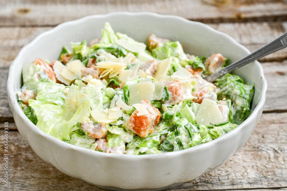 Homemade traditional Caesar Salad with Parmesan Cheese and Croutons in a white bowl on a old white table with leaves and a sauce boat Homemade traditional Caesar Salad with Parmesan Cheese and Croutons in a white bowl on a old white table with leaves and a sauce boat