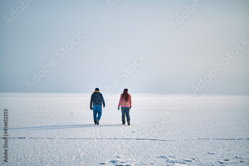 A guy and a girl are walking on a frozen lake