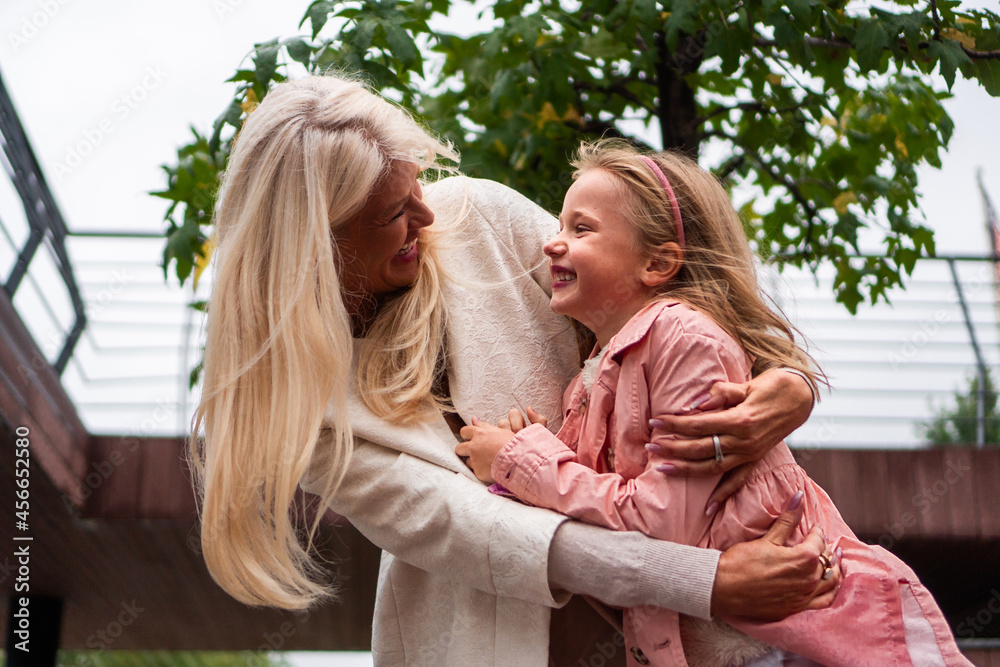 A good-looking, modern grandma and granddaughter hug and enjoy together while spending time outdoors on a cloudy, windy day.