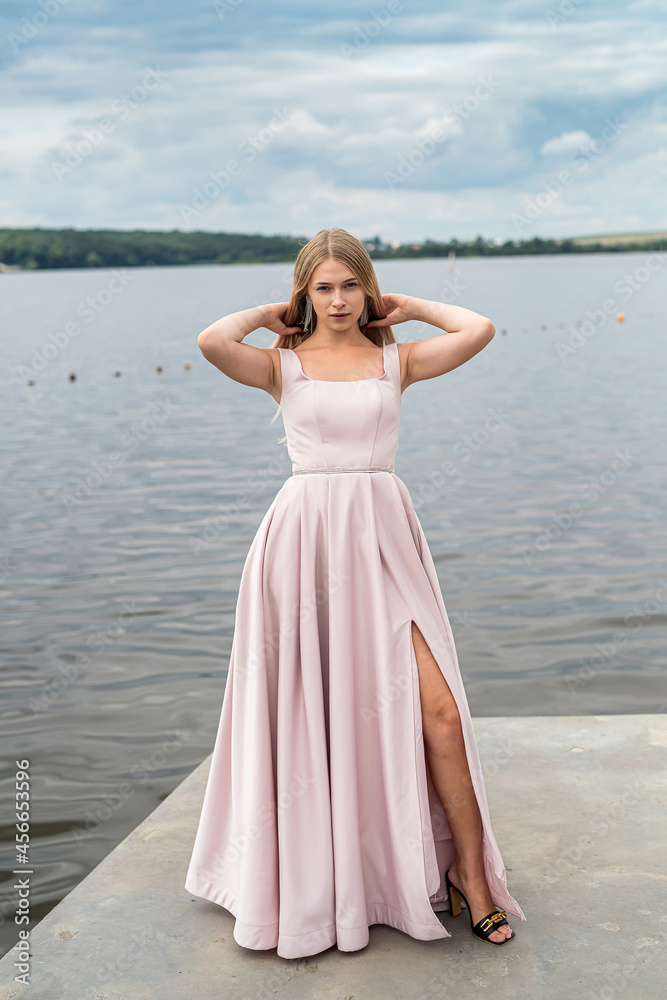 Pretty young woman wear in pink fashion evening dress posing near lake in the park Pretty young woman wear in pink fashion evening dress posing near lake in the park