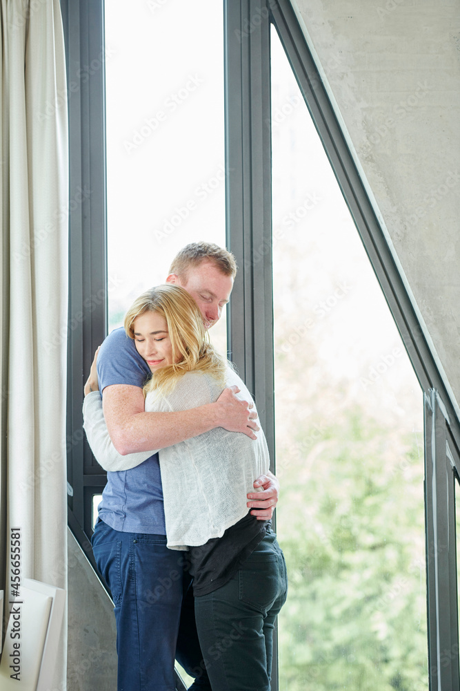 Happy young couple in love hugging at big window Happy young couple in love hugging at big window