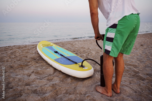 Close up of man prepares to paddle surf on a beach inflating sup board