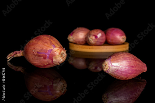 Group of five whole shallot on bamboo coaster on black glass