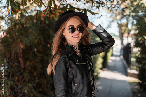 Happy portrait of a beautiful young girl model in fashionable clothes look with a leather jacket and stylish sunglasses walks in the autumn park