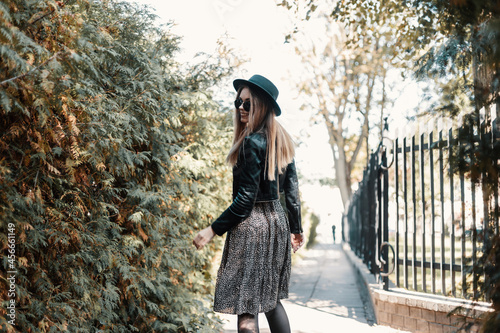 Pretty stylish smiling woman in fashion outfit look with leather jacket and vintage dress walks outdoors