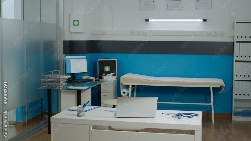 Nobody in doctors office with modern funiture at medical facility. Empty examination cabinet for healthcare specialist. Close up of white desk with laptop, stethoscope and pens Nobody in doctors office with modern funiture at medical facility. Empty examination cabinet for healthcare specialist. Close up of white desk with laptop, stethoscope and pens